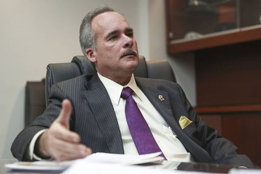 John Fleming - About John M. Fleming: A middle-aged man in a suit and tie sits at an office desk, gesturing with one hand while speaking. - Charlotte County Commissioner