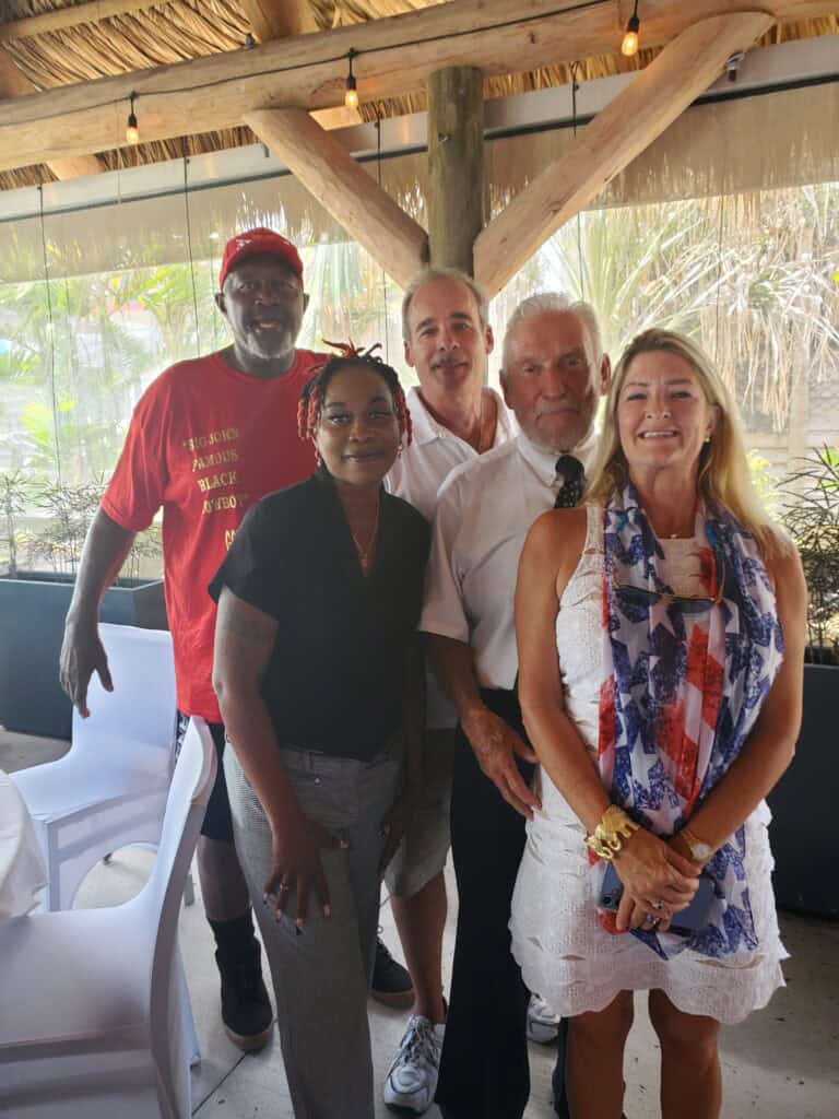 John Fleming - Five adults pose together indoors near a table under a thatched roof, with natural light and greenery in the background—capturing a relaxed moment that could be part of an About John M. Fleming gathering. - Charlotte County Commissioner